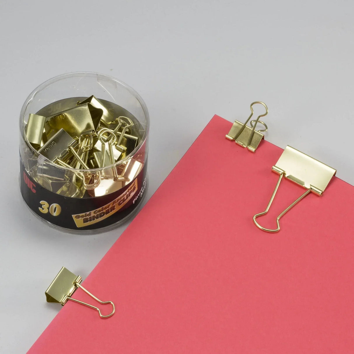 Gold binder clips holding pink paper, assorted sizes in clear container for office organization