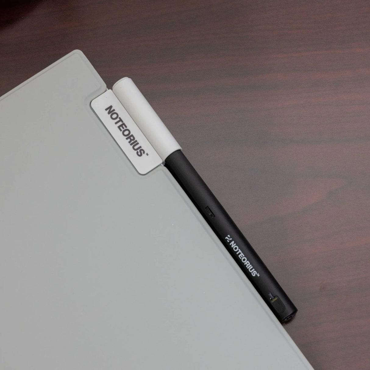 Magnetic black and white stylus pen attached to gray tablet labeled NOTeORIUS on wooden desk
