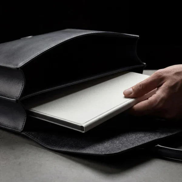 Person placing a white digital smart notebook into a black leather bag on a desk