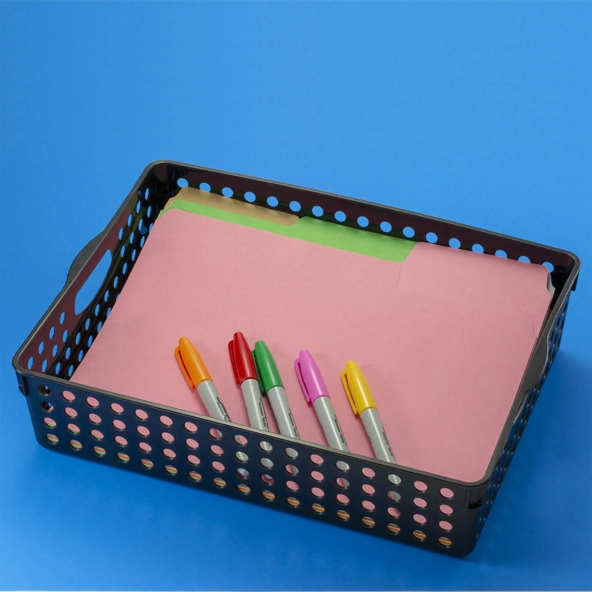 Black plastic office storage basket with folders and colorful markers on blue background
