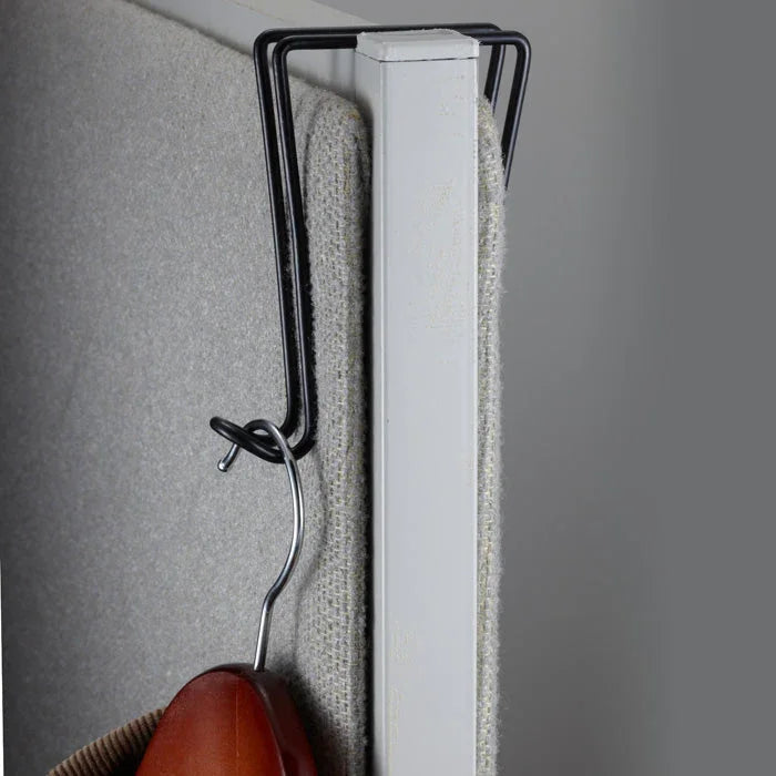 Black wire cubicle hook hanging over fabric-covered office partition, holding a coat hanger.