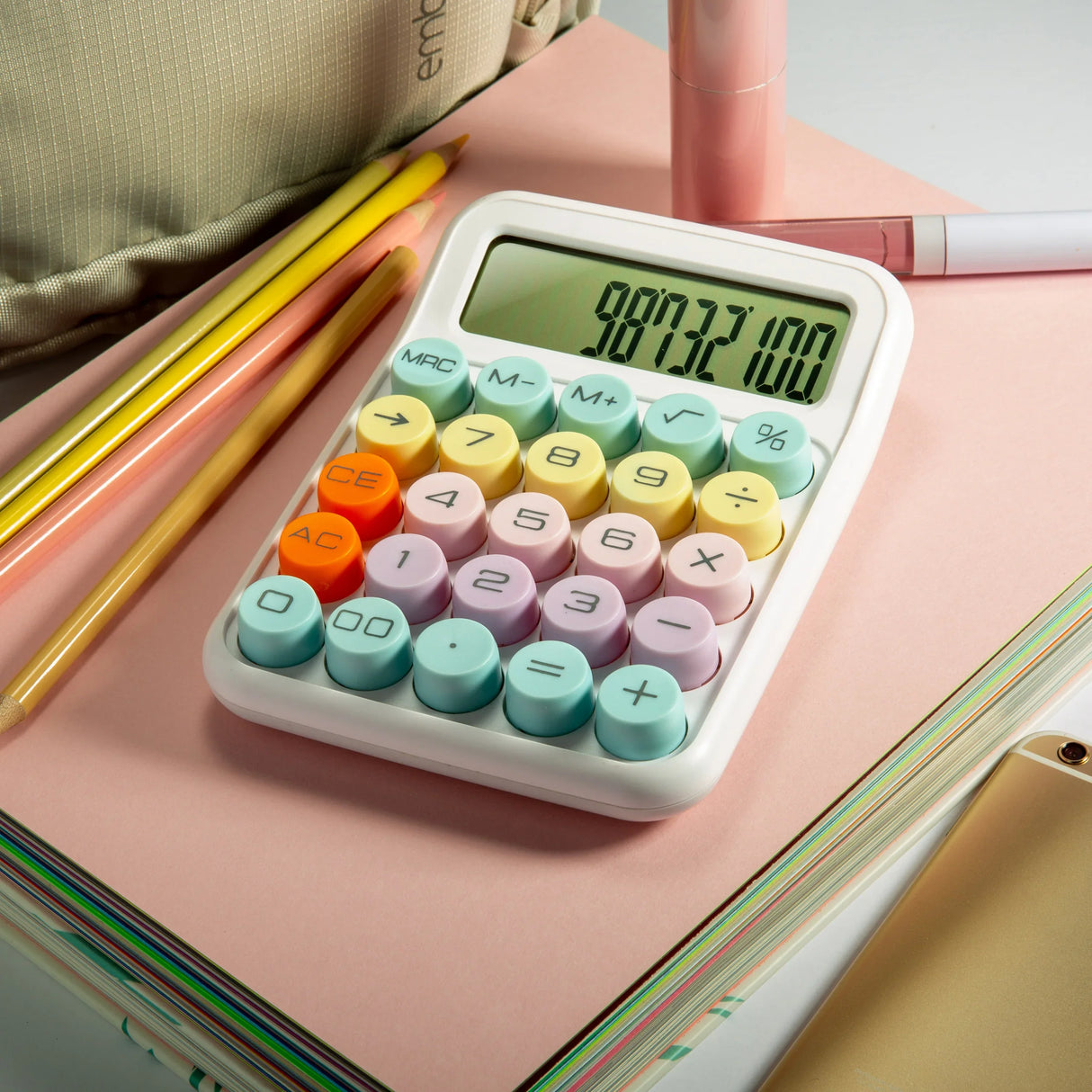 Colorful desktop calculator with round pastel buttons on notebooks, surrounded by pencils and stationery.