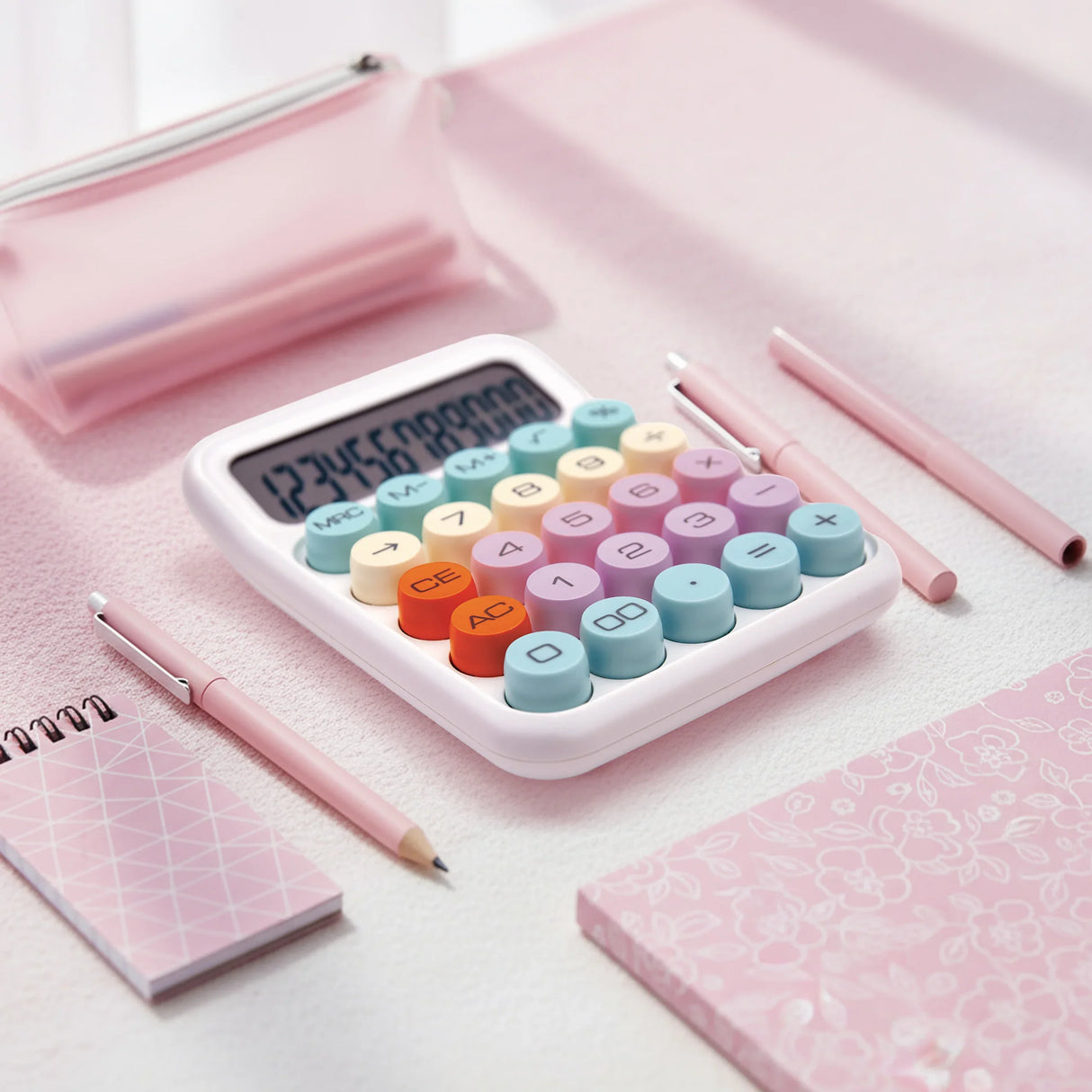 Colorful desktop calculator with round buttons on a pink workspace, surrounded by stationery.
