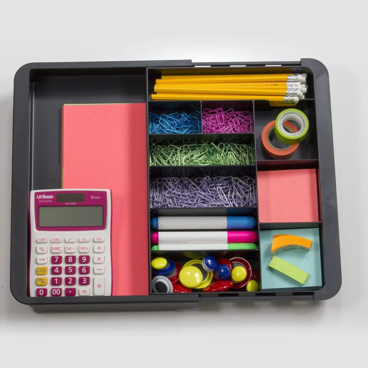 Expandable desk drawer tray filled with office supplies including a calculator, pencils, sticky notes, paper clips, markers, push pins, and tape.