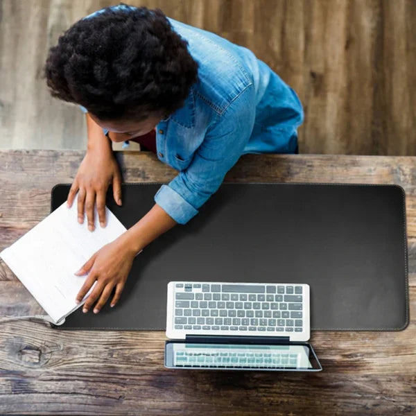 Person working at a rustic desk with a large black grounding desk pad, keyboard, and tablet.