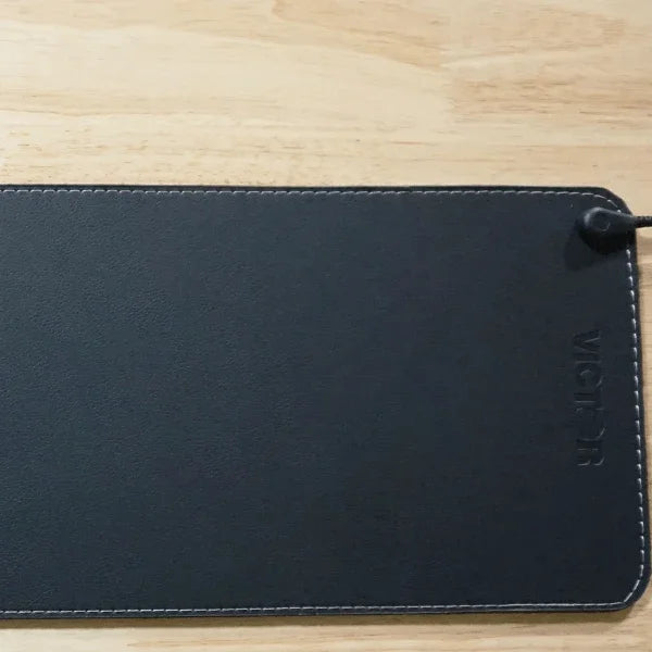Small black Victor® Grounding Desk Pad with stitched edges on a wooden surface