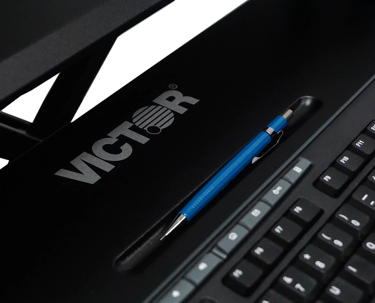 Close-up of black adjustable standing desk with keyboard tray, pen slot, and visible keyboard.