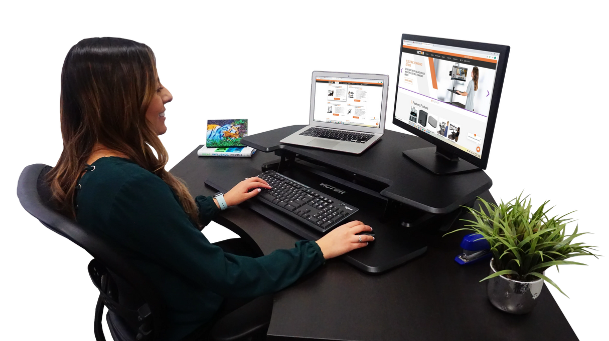 Woman using an adjustable standing corner desk with monitor, laptop, keyboard and office accessories