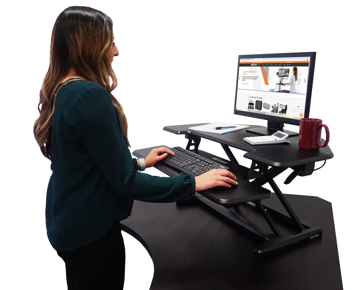 Woman working at a high-rise adjustable corner standing desk with monitor and keyboard tray