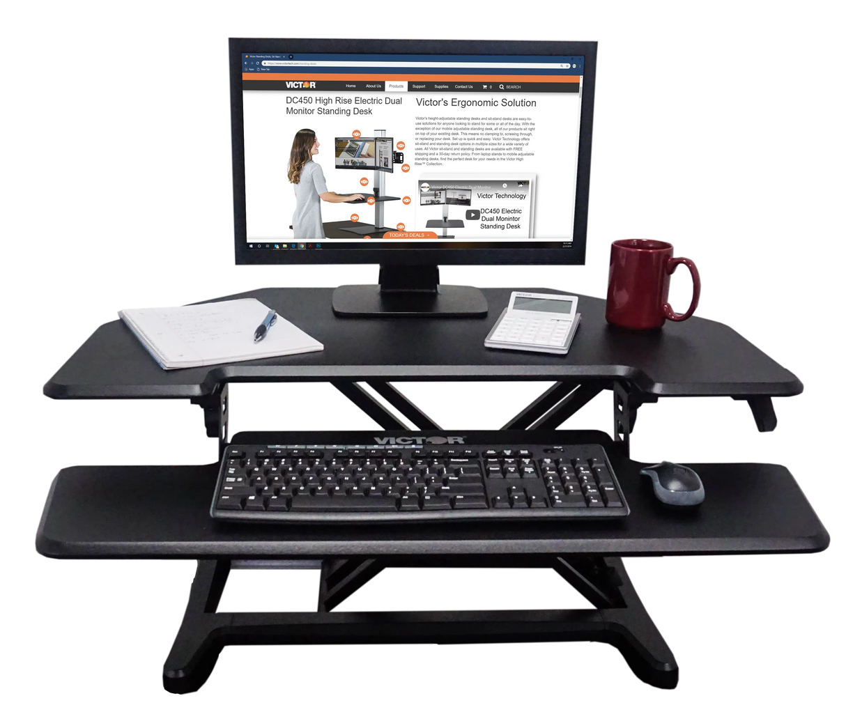 Adjustable corner standing desk with monitor, keyboard tray, coffee mug, notebook, and calculator