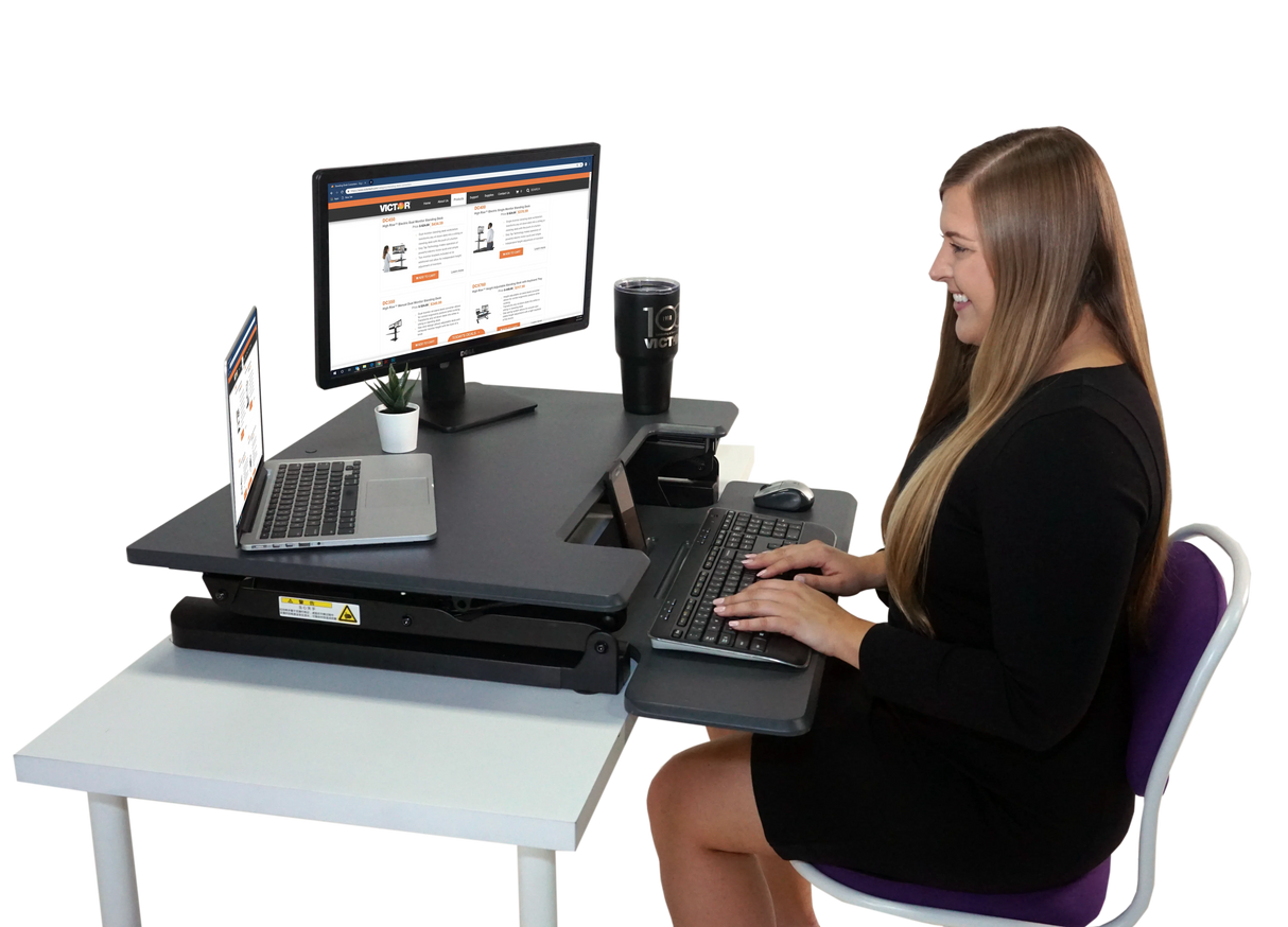 Woman using high-rise adjustable standing desk with computer, laptop, and office accessories