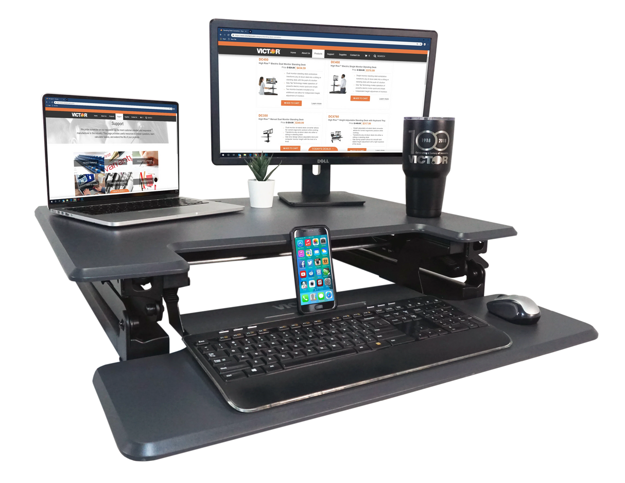 Adjustable height standing desk with monitor, laptop, keyboard, mouse, smartphone, and tumbler