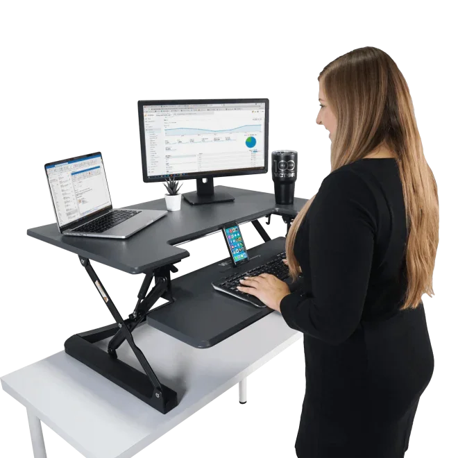 Woman using adjustable standing desk with monitor, laptop, keyboard tray and phone holder