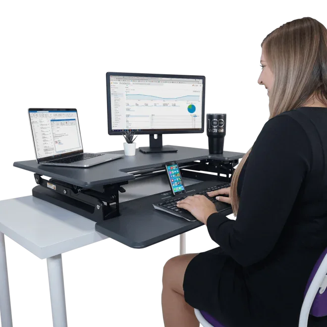 Woman using high rise adjustable standing desk with dual monitor setup and keyboard tray
