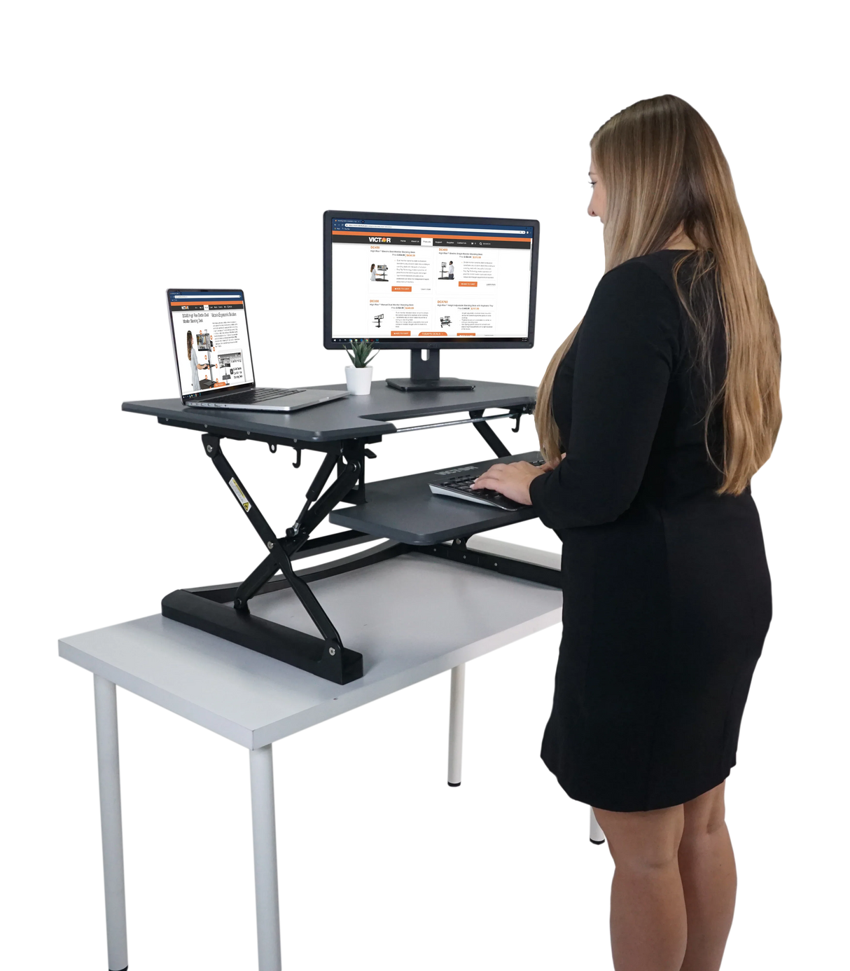 Woman using an adjustable height standing desk with keyboard tray, monitor, and laptop
