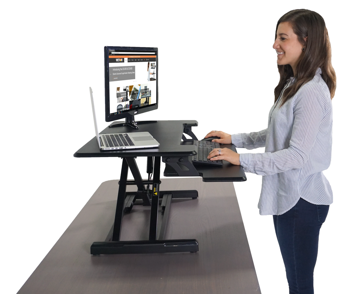 Woman using an adjustable height standing desk with keyboard tray and dual monitor setup