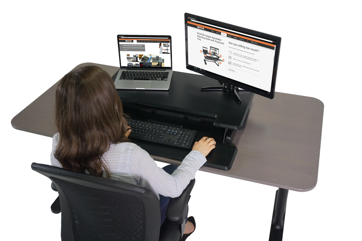 Woman working at high-rise adjustable standing desk with monitor, laptop, and keyboard tray