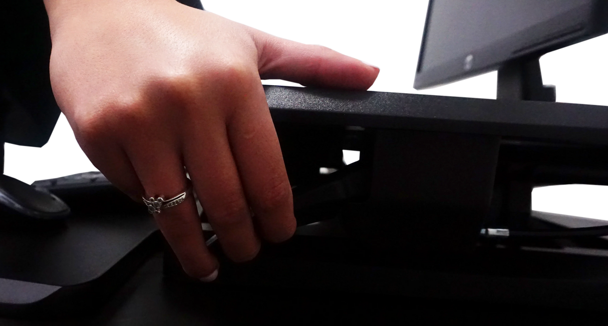 Hand adjusting height lever on compact standing desk with keyboard tray and monitor