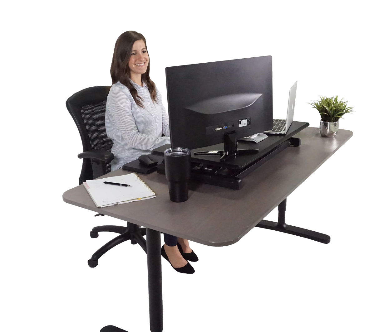 Woman working at an adjustable height standing desk with monitor, laptop, and office accessories
