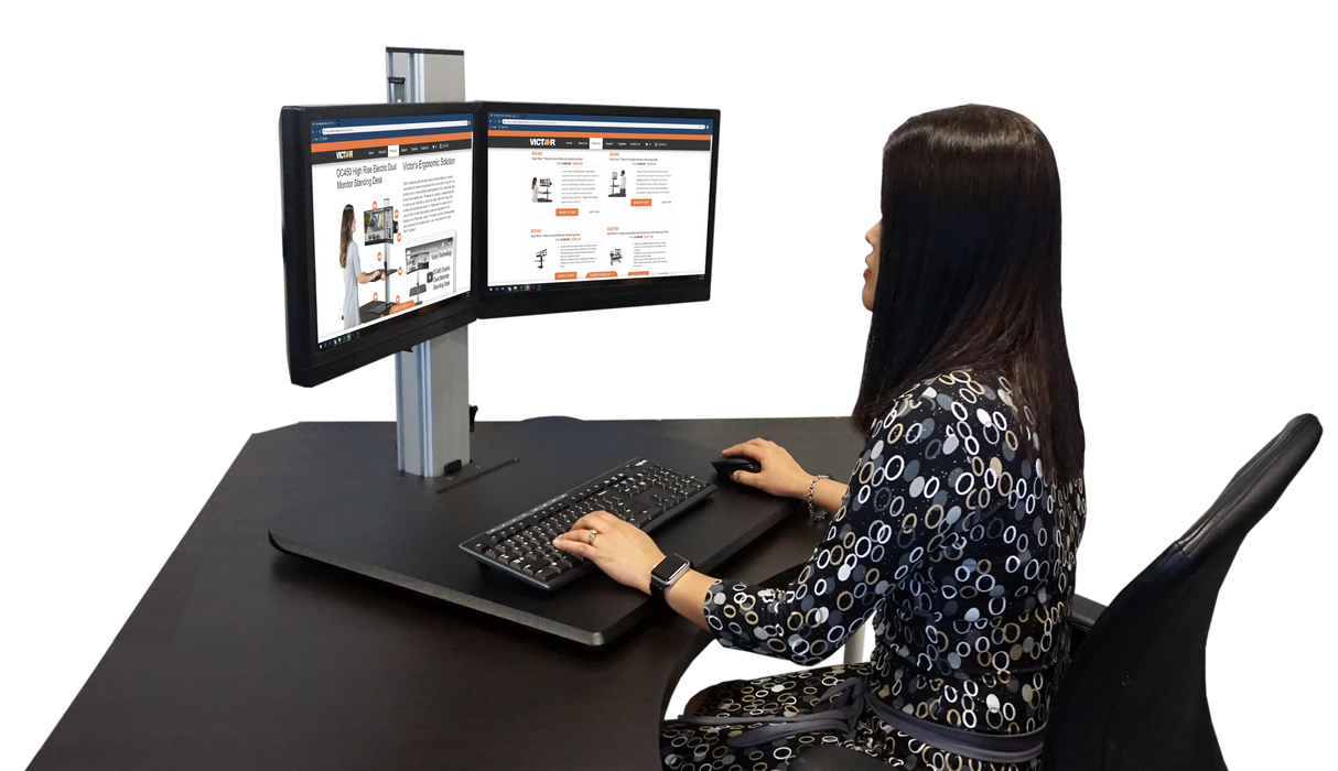 Woman working at a dual monitor standing desk with keyboard and mouse in modern office setup