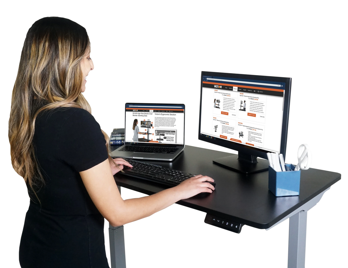 Woman using electric adjustable standing desk with dual monitors in modern office setup