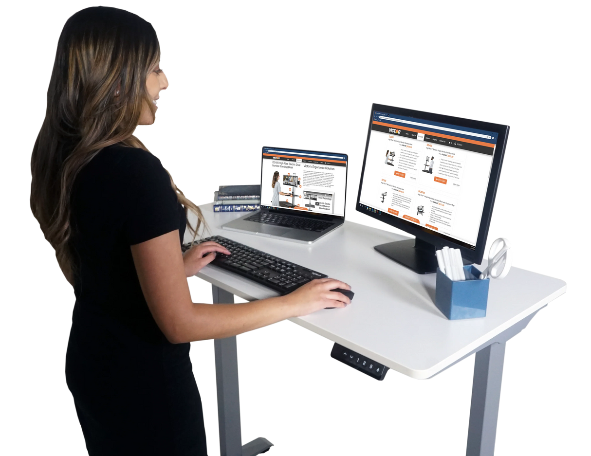Woman working at an electric adjustable height standing desk with monitor and laptop