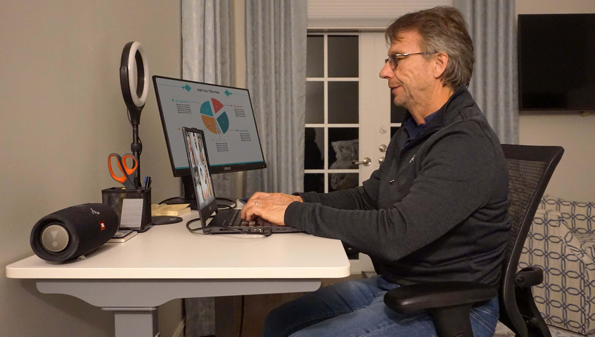 Man working at electric adjustable height standing desk with dual monitors in home office