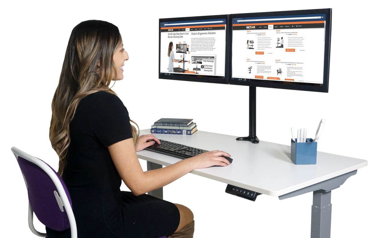 Woman working at electric adjustable height standing desk with dual monitors