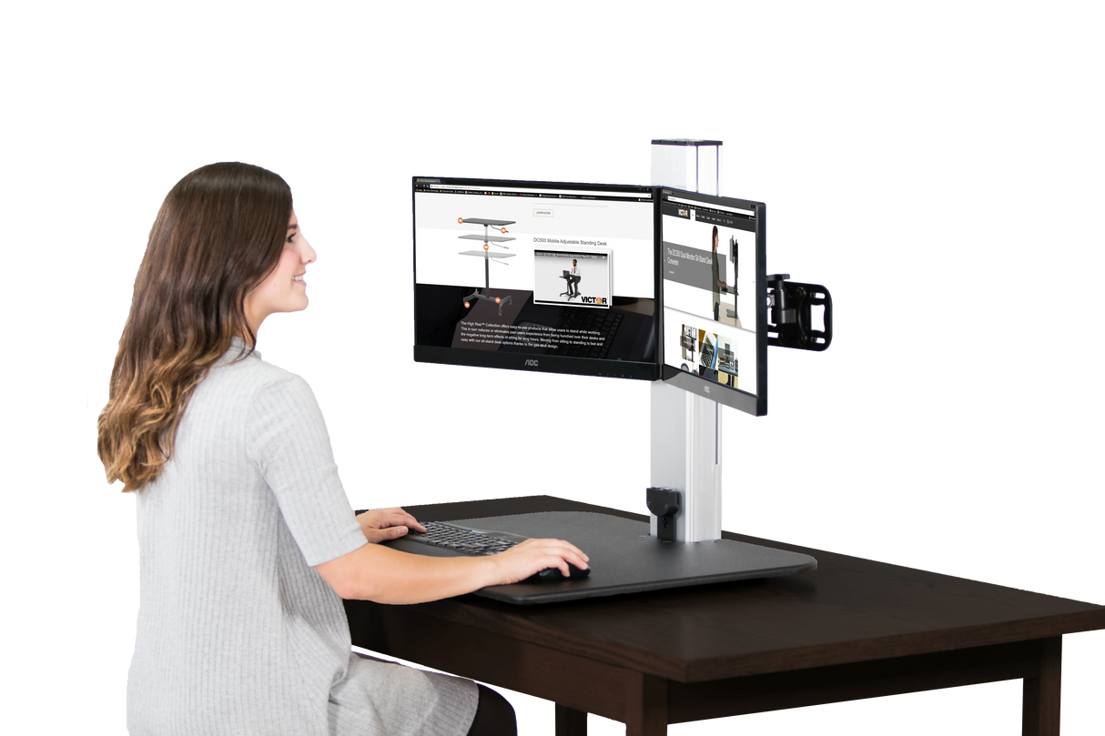 Woman at desk using electric dual monitor standing desk workstation