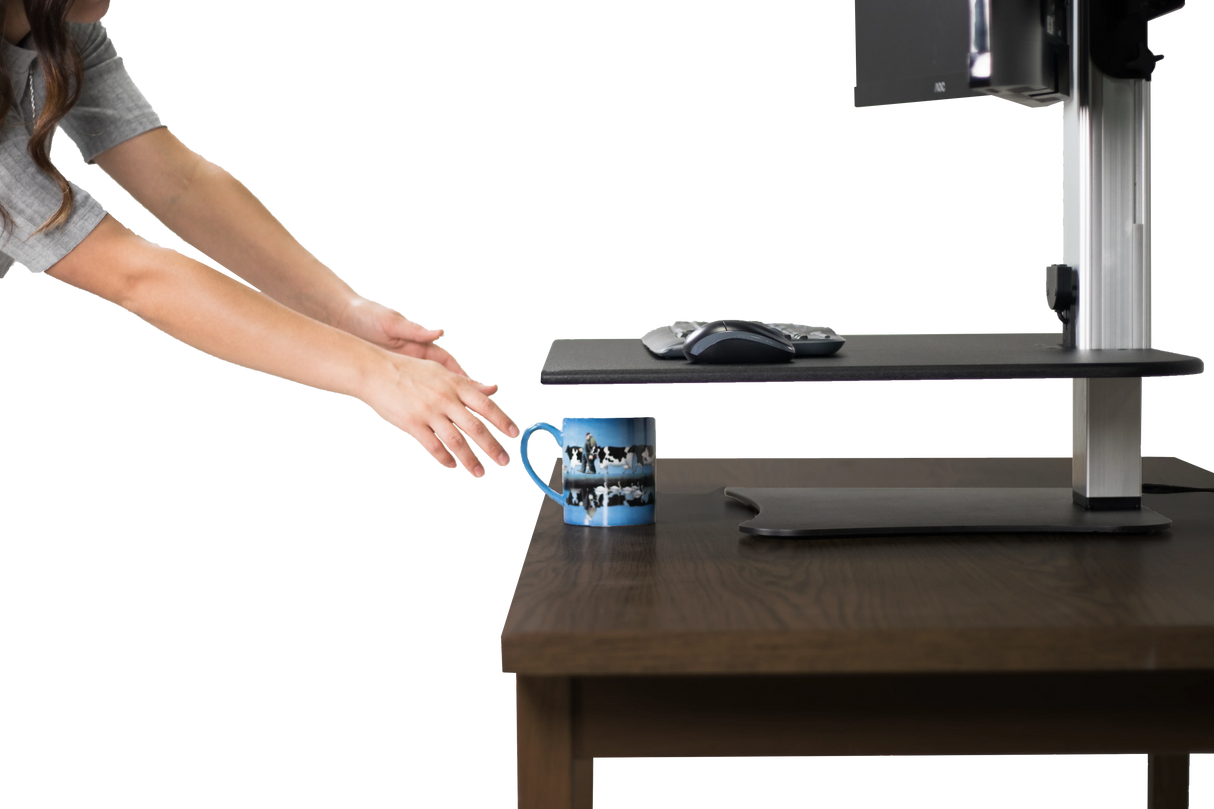 Hands reaching for a coffee mug on wood desk with an electric dual monitor standing desk setup