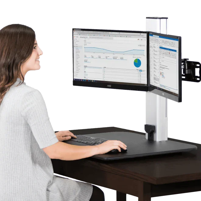 Woman working at a high-rise electric standing desk with dual monitors in office setting