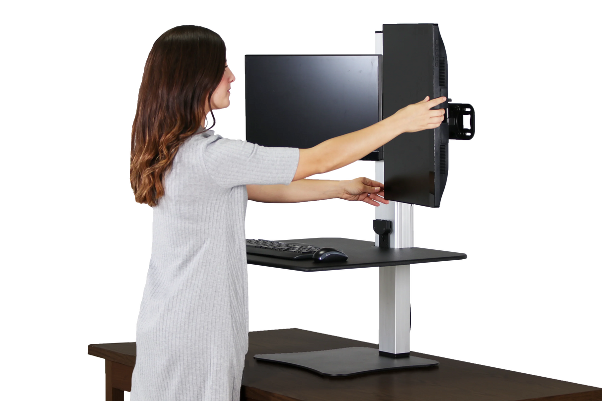 Woman adjusting dual monitors on electric height-adjustable standing desk converter