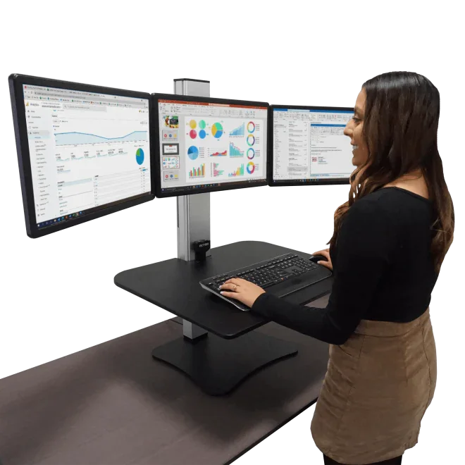 Woman using high-rise electric standing desk with triple monitors and keyboard tray