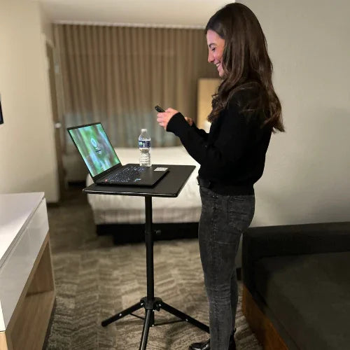 Woman using a high-rise mobile tripod standing desk with laptop in a modern room