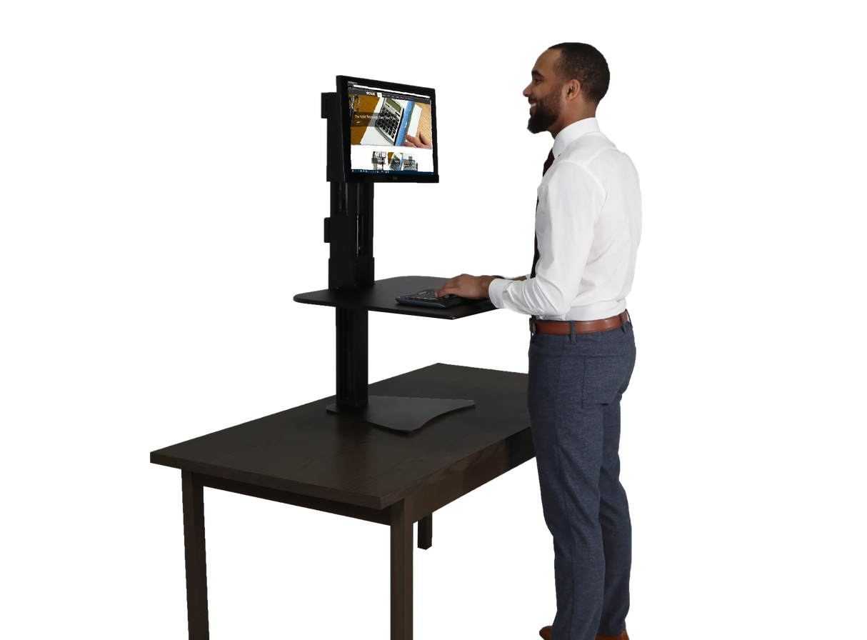 Man using a high-rise single monitor standing desk workstation on a wooden table