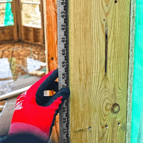 A person in red gloves using a Victor ProSpan magnetic measuring tool on a wooden beam.
