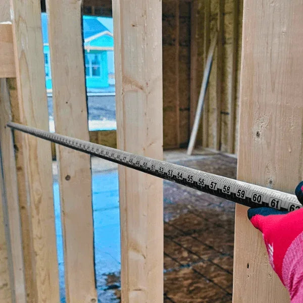 A person holds a Zip Stick 144" ProSpan Magnetic Measuring Tool against wooden framing.