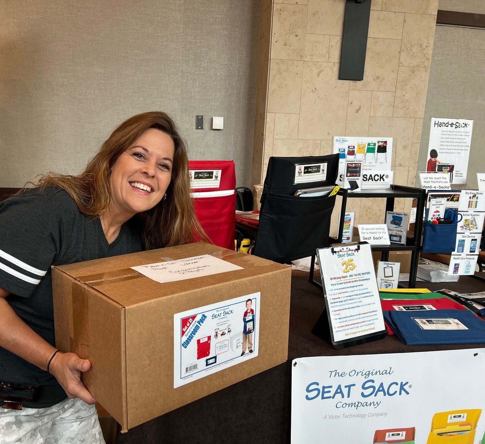 Smiling teacher holding Seat Sack classroom pack box at a display table with seat organizers