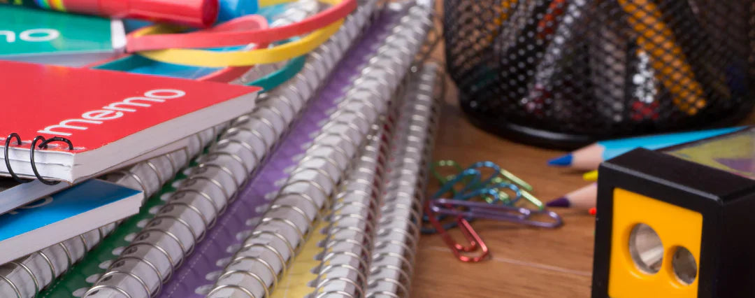Assorted school supplies including notebooks, memo pads, colored pencils, and paper clips on a desk