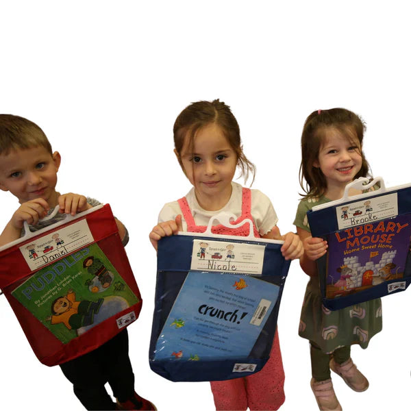 Three young children holding colorful book bags with picture books, smiling and standing together.