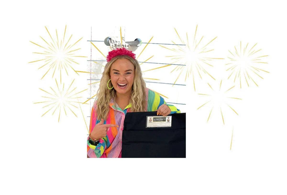 Smiling woman in colorful shirt holding black Seat Sack organizer with fireworks background