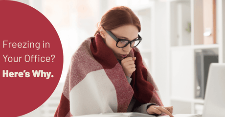 Cold woman wrapped in a blanket and wearing glasses working at an office desk.