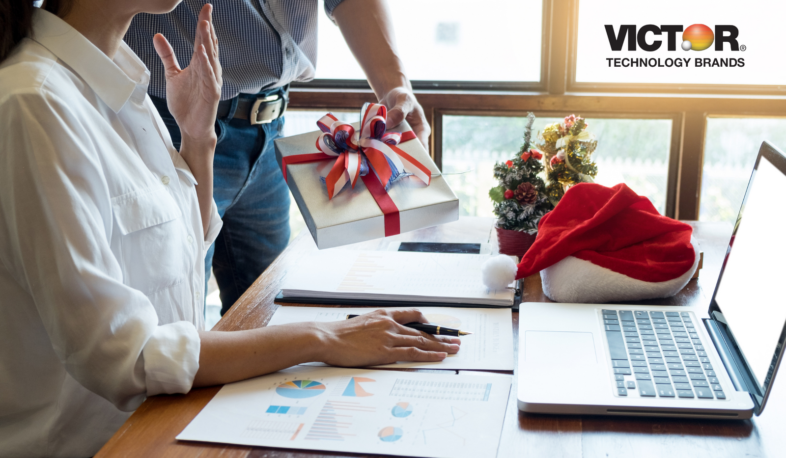 Office holiday gift exchange with charts, laptop, Santa hat, and festive decor on desk