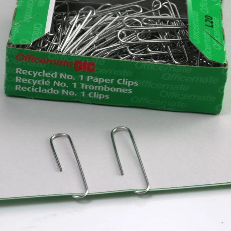 Box of large recycled paper clips with two silver paper clips on a gray surface