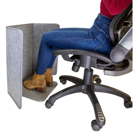 Woman using a grey foot and leg heater under desk for ergonomic office comfort