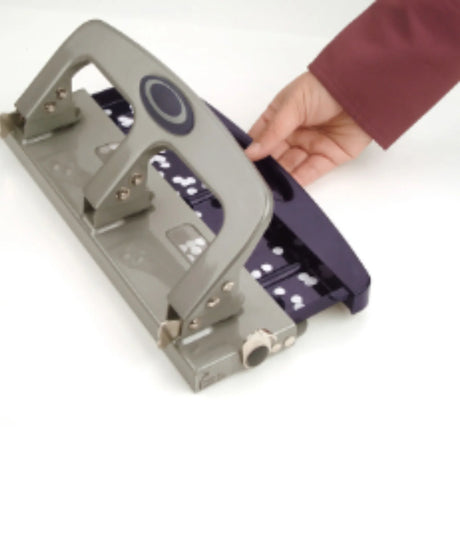 Metal three-hole punch for office paper, with handle and hand adjusting tray, on white background.