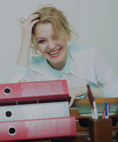 Smiling woman at desk with red binders, pens, and office supplies, office setting