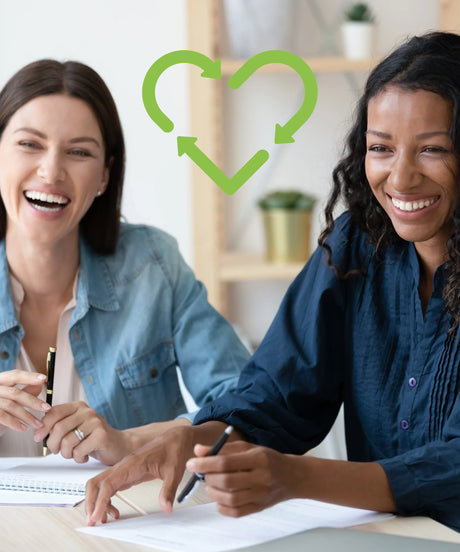 Two women in office setting smiling with green recycle heart icon, sustainable office products