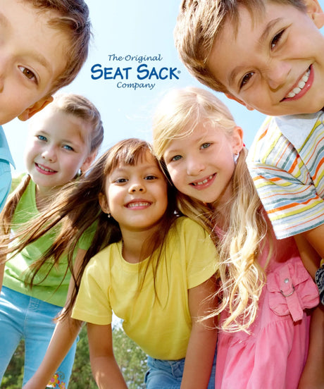 Group of smiling children outdoors under Seat Sack Company logo, colorful clothing, sunny day