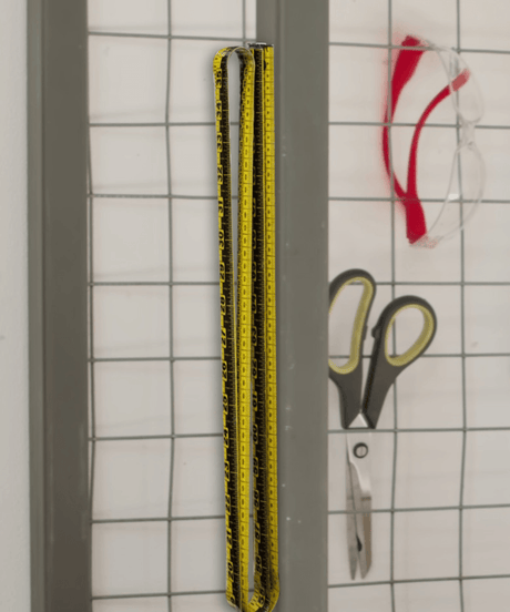 Yellow measuring tape, scissors, and safety glasses on grid wall for workspace organization